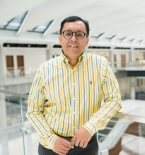 A photo of Navid Saleh, a man with dark hair and glasses, standing and smiling in a striped yellow button up shirt.