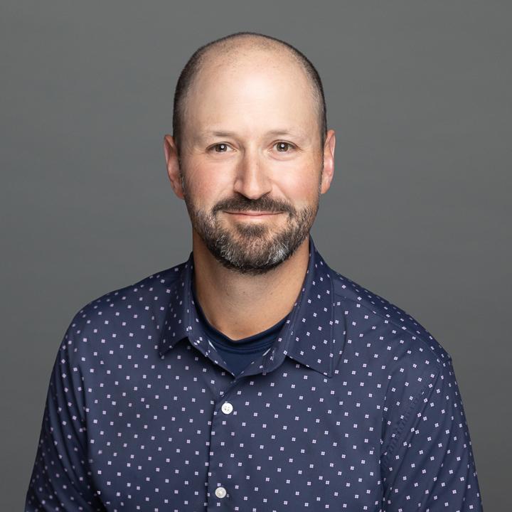 A headshot of Steve Finkelstein, a white man with a dark brown mustache and beard, in a blue button up dress shirt.