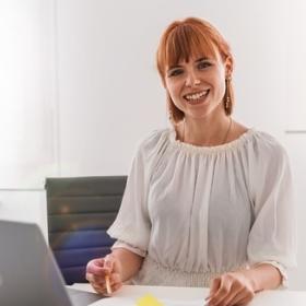 Woman with laptop, pen, and paper looking at camera