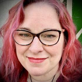 Smiling individual wearing glasses and rose colored hair